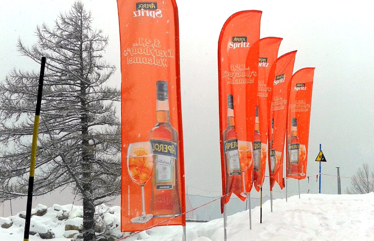 Bandiere Aperol Spritz lungo un percorso innevato